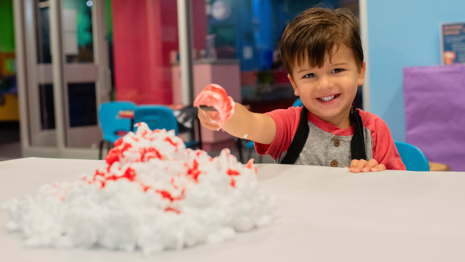 Child smiling as they dip their paintbrush in a pile of shaving cream.