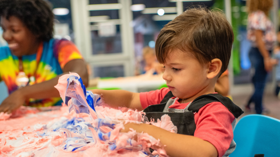 Close up of child in a smock and playing in shaving cream.
