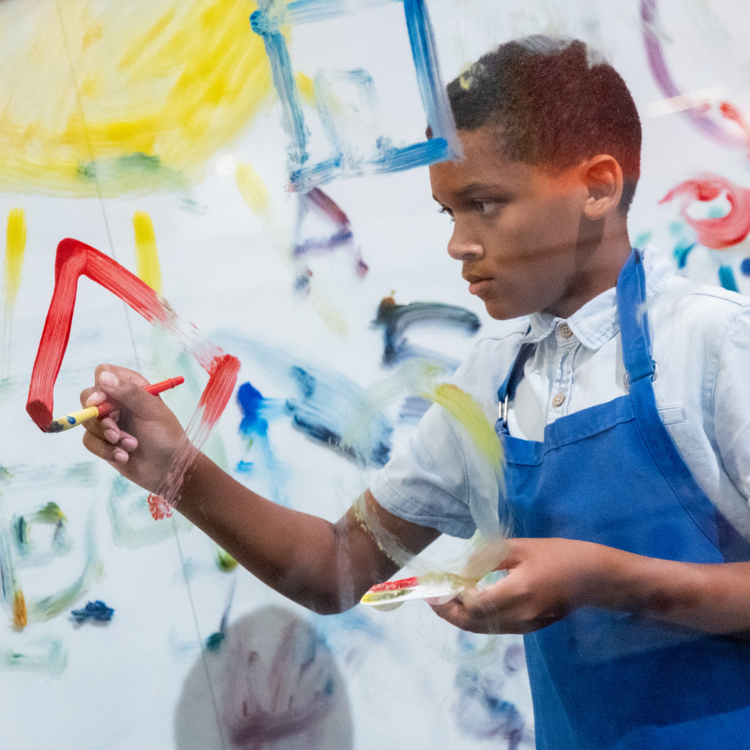 Kid at Paint Wall wearing apron and painting