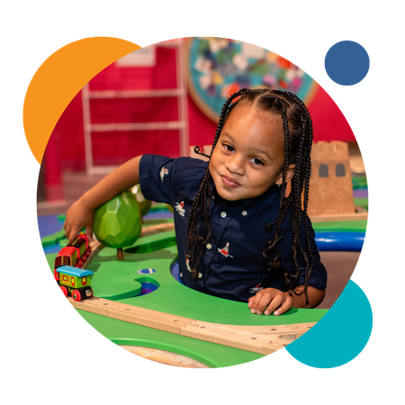 Image of child playing with a train and train tracks at the Museum's Gateway to the World exhibit.