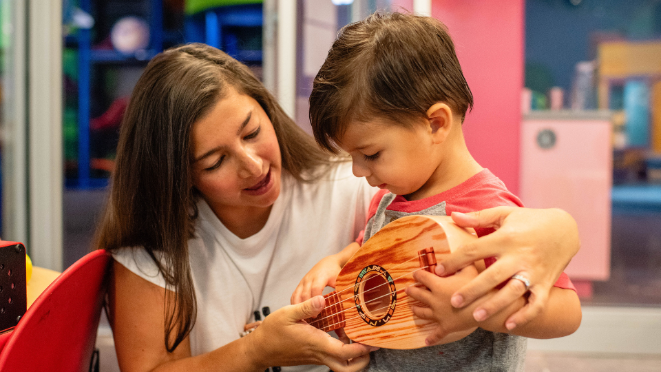 Caregiver and child playing ukulele together